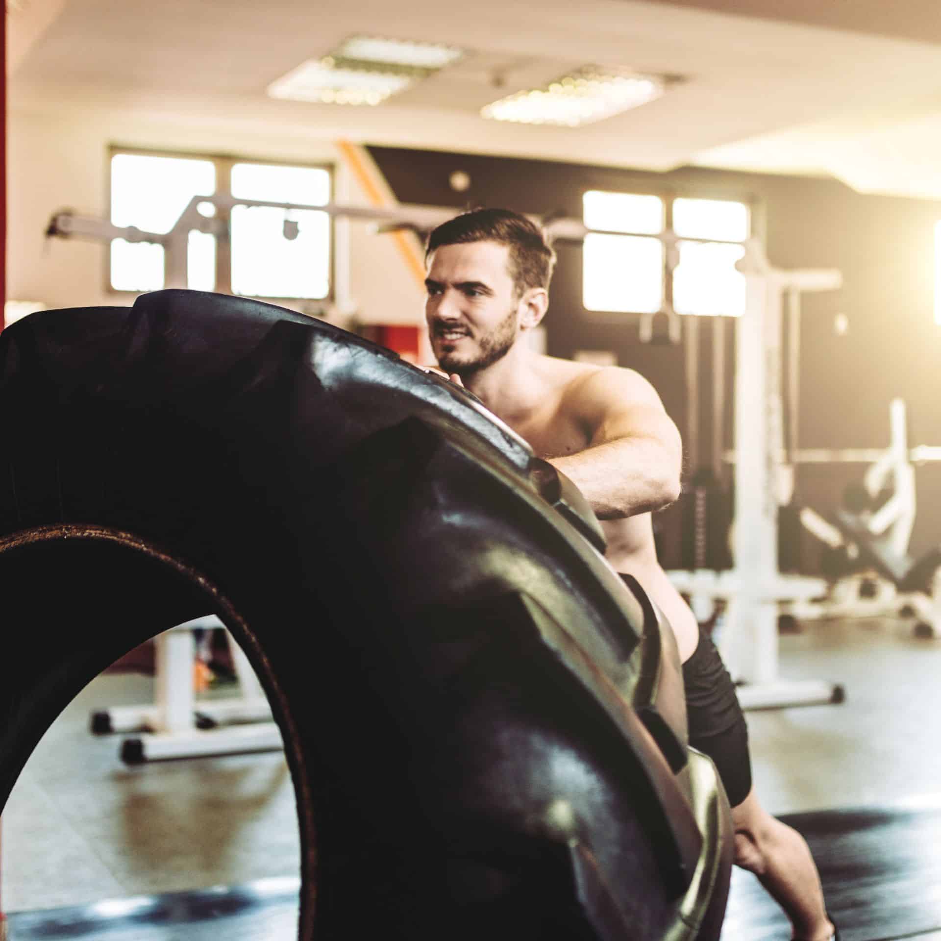 A man flipping a large tire in a gym as part of a fitness workout.