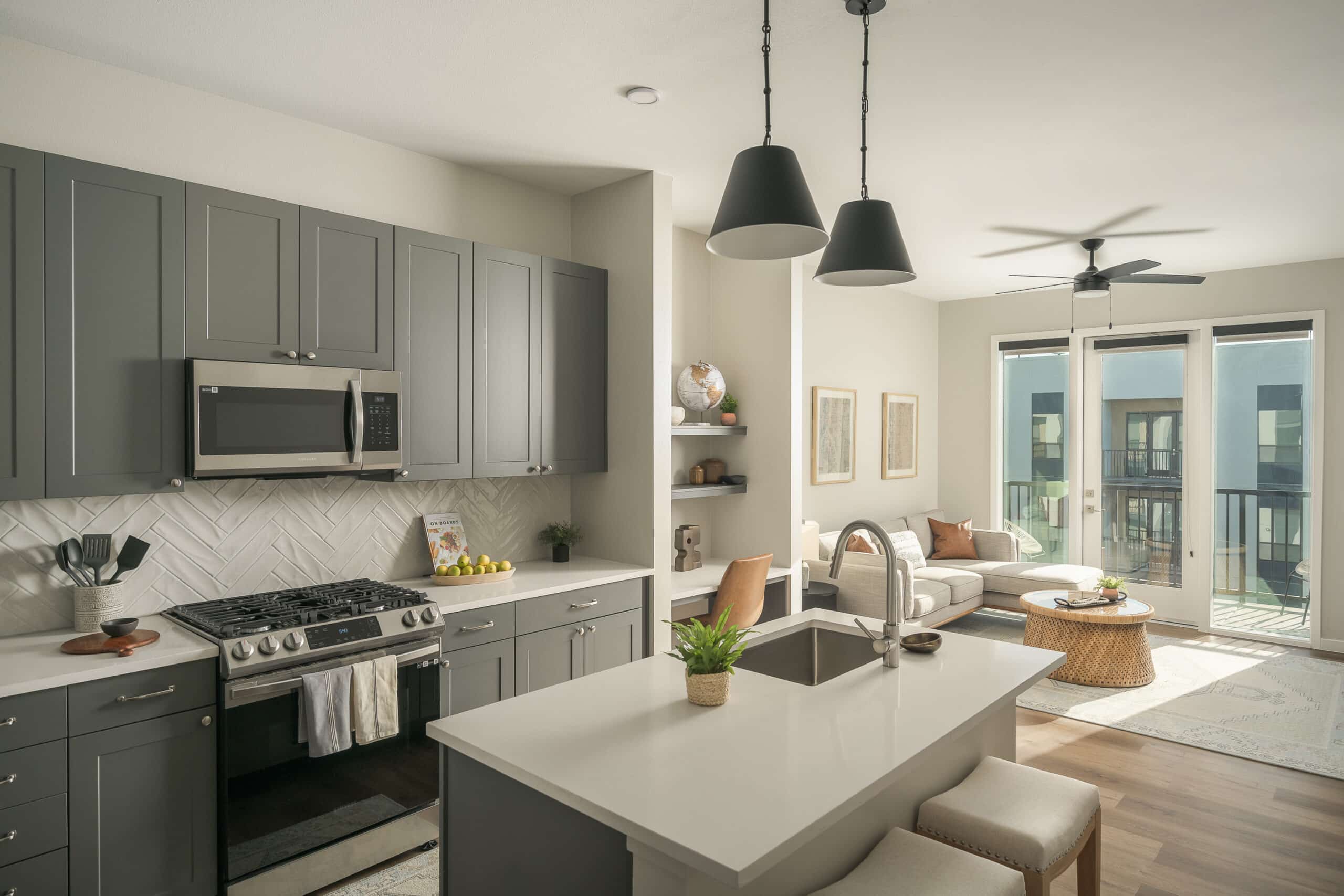 Bright kitchen interior with clean lines, featuring gray cabinetry, stainless steel appliances, a white countertop, and pendant lighting.