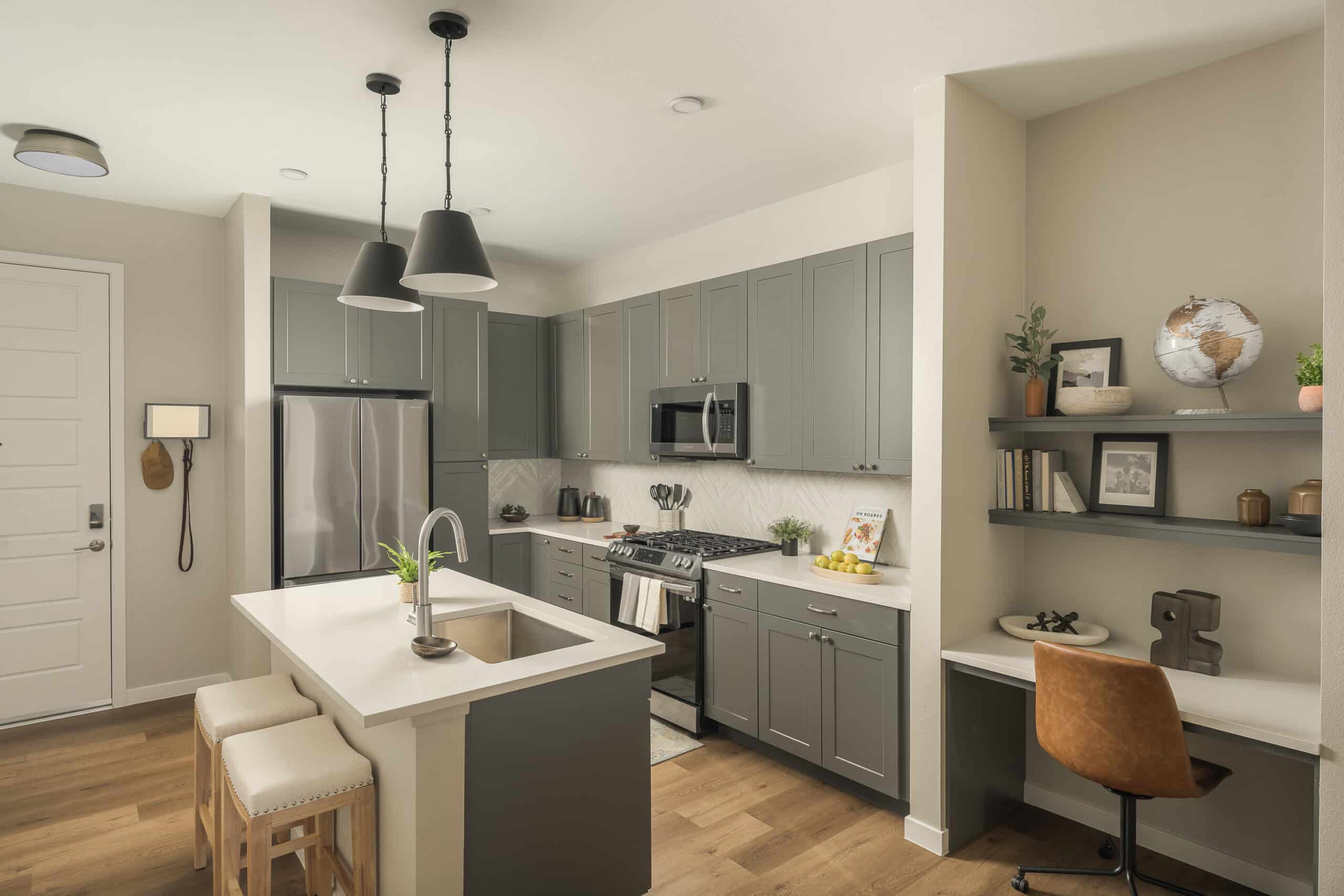 Modern kitchen interior with gray cabinets, stainless steel appliances, and a central island with bar stools.